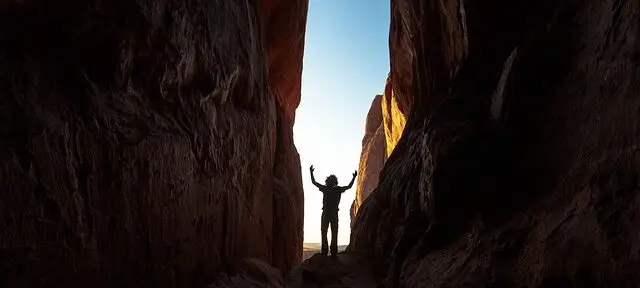 un homme à l'aube lève les bras entre deux montagnes